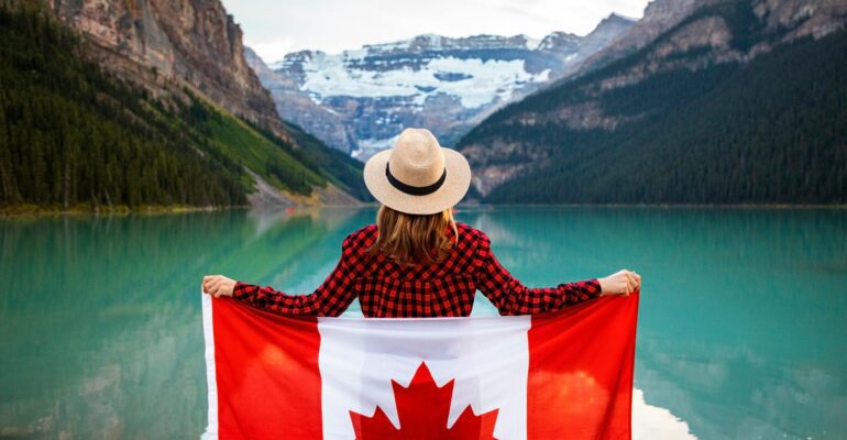 Woman holding a Canadian flag at stunning Lake Louise, Alberta, embracing nature and patriotism.